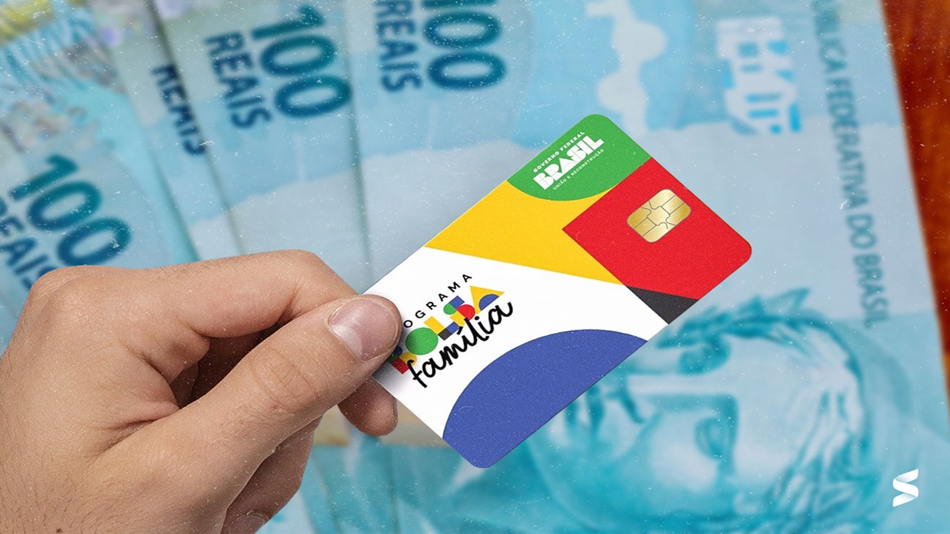 Cédulas de cem reais, na cena, uma mão segurando o cartão do bolsa família